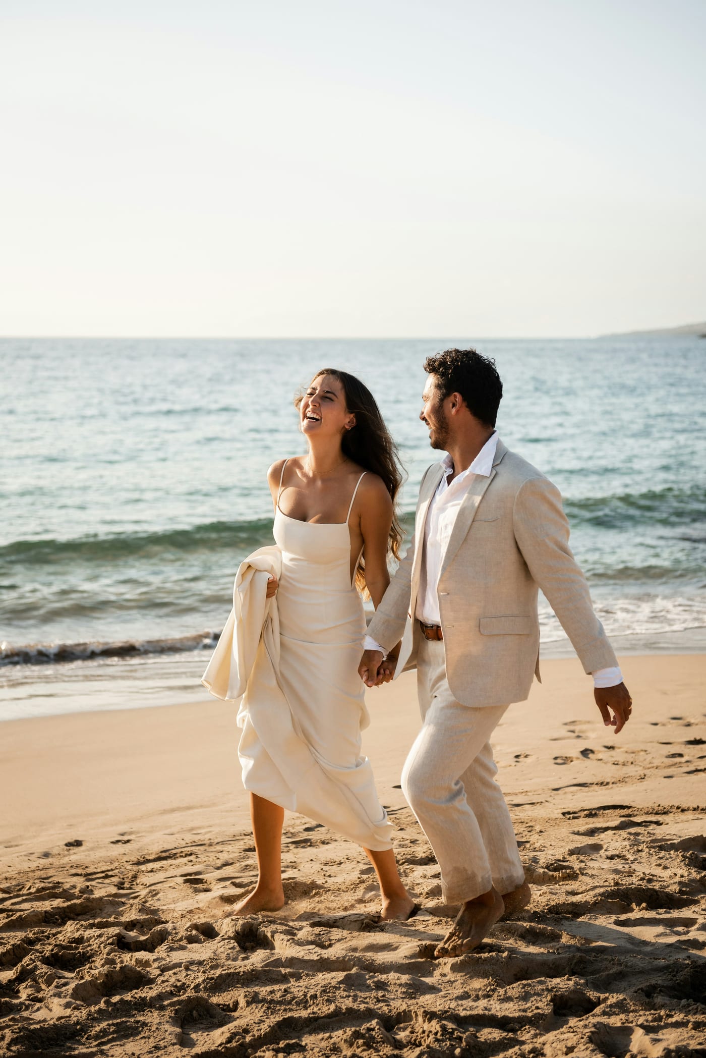 A couple walking barefoot along the shoreline at golden hour after their ceremony