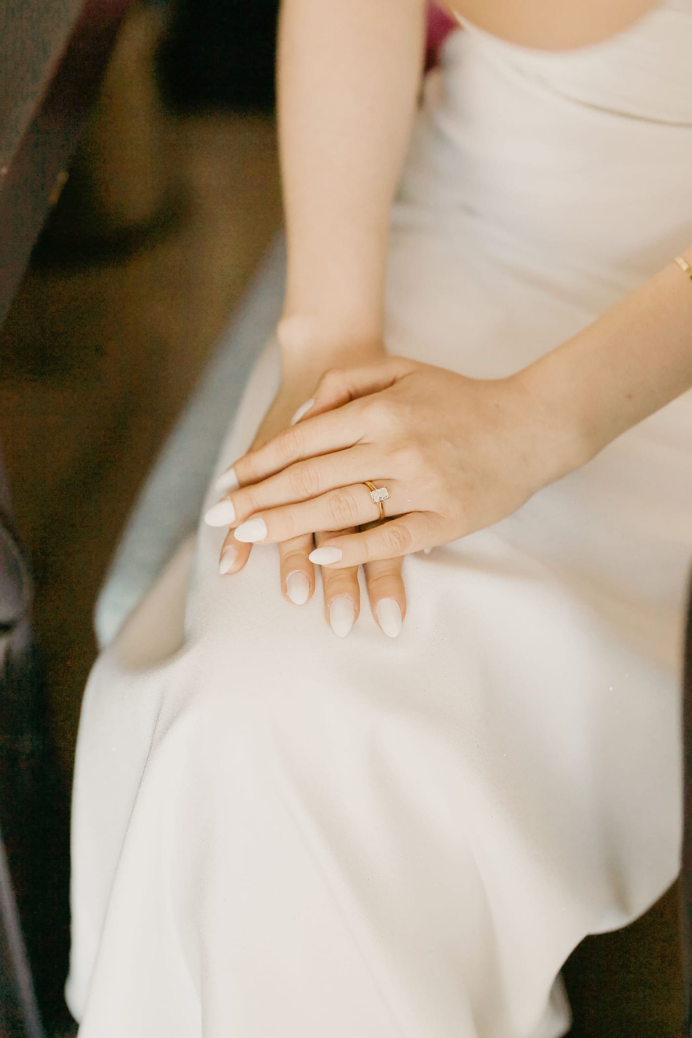A bride’s hands resting in her lap, her engagement ring catching the light