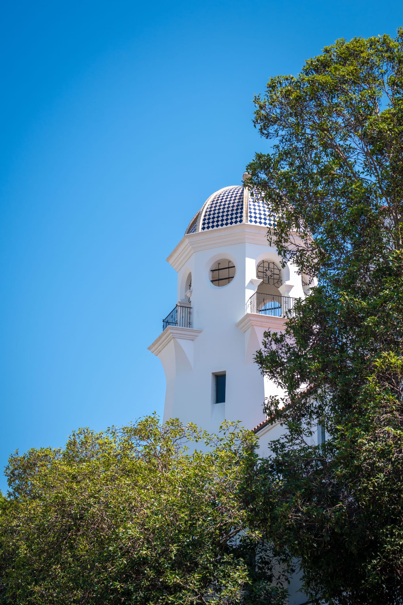 A white Spanish Colonial tower with a tiled dome rising above the treetops in Santa Barbara